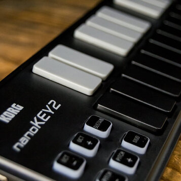 Detailní záběr na černý MIDI kontrolér s klávesami. Na povrchu je bílým písmem uveden název značky KORG a model nanoKEY2. Jsou vidět bílé a černé klá…