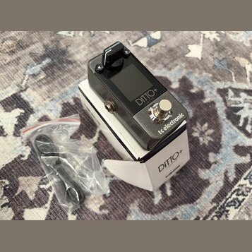 Černý kytarový pedál s nápisy DITTO+ LOOPER a tc electronic v kovovém šasi. Zařízení leží na bílém originálním krabici s identickými nápisy DITTO+ LO…