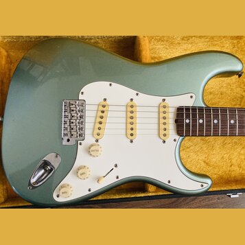 Světle zelená elektrická kytara typu Stratocaster s bílým pickguardem a třemi jednoduchými snímači. Nástroj je umístěn v otevřeném kufru s žlutým pol…