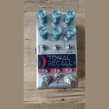 Stříbrný efekt pedál s nápisem TONAL RECALL ANALOG DELAY a červeným logem ve tvaru půlměsíce. Zařízení má šest modrých kovových oválů s popisky TONE…