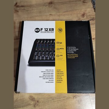 Fotografie znázorňuje krabici od míchací konzole s nápisem RCF F 12 XR PROFESSIONAL MIXING CONSOLE. Na obalu je vyobrazen černý mixážní pult a texty…