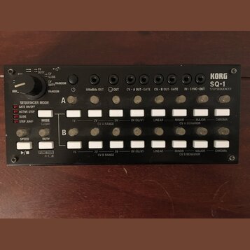 Černý sekvencer KORG SQ-1 STEP SEQUENCER s kovovým povrchem. Zařízení obsahuje dvě řady bílých tlačítek, několik ovládacích knofíků a řadu výstupů s…