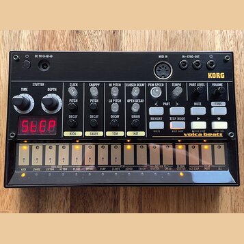 Černý elektronický drum machine s nápisem KORG a modelem volta beats. Zařízení obsahuje červený digitální displej, řadu bílých tlačítek a ovládacích…