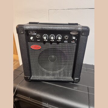 Černý kytarový kombo zesilovač s texturovaným povrchem a kovovou mřížkou reproduktoru. Na ovládacím panelu jsou nápisy CA-15 Guitar Amplifier, Drive,…
