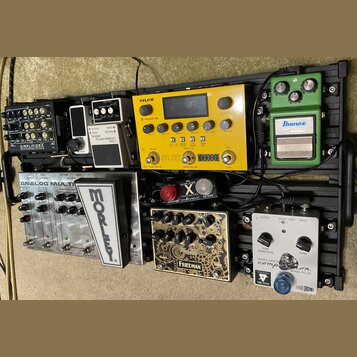 Sestava efektů na černém pedalboardu. Horní řada obsahuje pedály s nápisy SIMPLIFIER X, BOSS Noise Suppressor NS-2, žlutý procesor NUX s nápisem DUAL…