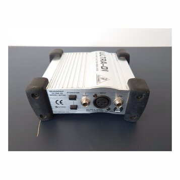 Stříbrná DI box s černými gumovými nárožníky. Na zadním panelu jsou nápisy BEHRINGER®, ULTRA-DI, MODEL DI100, ATTENUATION, INPUT a LINK, dále značka…