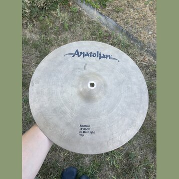 Kruhový činel z kovaného kovu s viditelným rýhováním povrchu. V horní části je nápis Anatolian a v dolní části text Emotion 14"/35cm Hi-Hat Light Top…