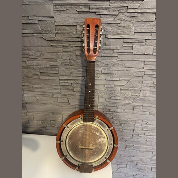 Akustický banjo s hnědým dřevěným tělem a krkem. Instrument má kovový, stříbrný rezonanční povrch s viditelnými šmouhama a oxidací. Na hmatníku jsou…