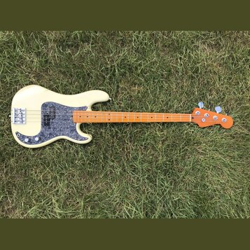 Elektrická basová kytara s krémovým korpusem a hnědým javorovým hmatníkem. Na korpusu je šedý pickguard s texturou mramoru a stříbrný most. Nástroj n…