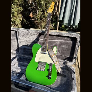 Zelená elektrická kytara typu T-style s bílým pickguardem v otevřeném hrdelním kufru. Na hlavě hmatníku je vidět nápis Fender. Kytara má připevněný v…