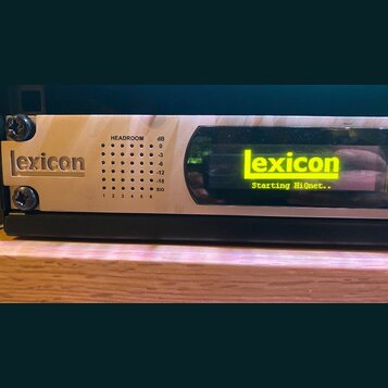 Detailní pohled na přední panel elektronického zařízení značky Lexicon. Na levé straně je nápis lexicon v obdélníkovém rámečku a vedle něj se nachází…