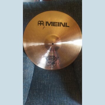 Zlatavý mosazný činel s jemným kruhovým broušením povrchu. Na horní části je černý nápis MEINL a pod ním menším písmem ROLAND MEINL spolu s logem. Ve…
