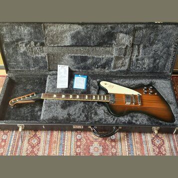 Elektrická kytara s černobrowným přechodem (sunburst) v hnědém tvrdém kufru s šedou vnitřní výplní. Na bílém pickguardu je viditelné logo Gibson. Kyt…
