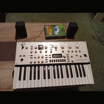 Bílý syntetizátor s klaviaturou, na kterém je vlevo nápis KORG a vpravo KingKORG NEO. Přístroj obsahuje řadu bílých otočných ovladačů, tlačítek a dva…