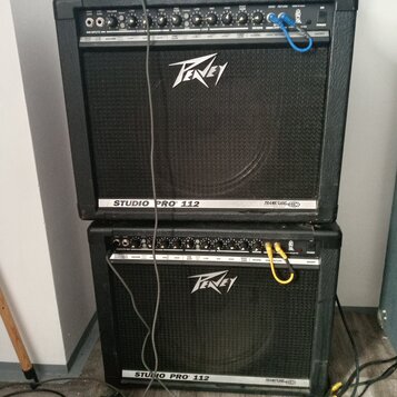 Dvě černé kytarové komba značky Peavey model Studio Pro 112, umístěná nad sebou. Na horním panelu obou zesilovačů jsou vidět ovládací knofíky, přepín…