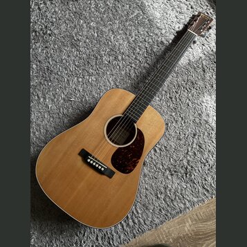 Akustická kytara s přirozeným dřevěným povrchem korpusu a tmavým hmatníkem. Na hlavě je vidět nápis "Yamaha". Kytara má tmavý plechtr ochránič s mram…