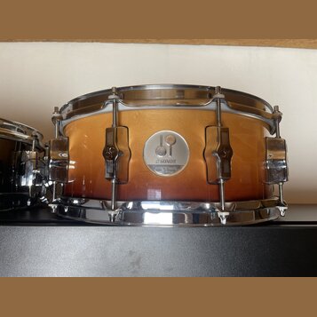 Zlatavý buben s přechodem do tmavě hnědé barvy v dolní části. Na korpusu je umístěn kulatý kovový štitek s nápisy SONOR, FORCE 3005 a 7 ply MAPLE. Ná…