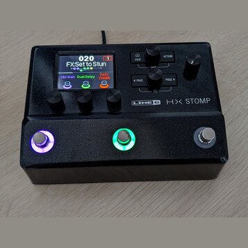 Černý efektový procesor Line 6 HX STOMP s kovovým povrchem v textuře glitter. Zařízení má digitální displej, čtyři ovládací knoflíky a tři nožní spín…