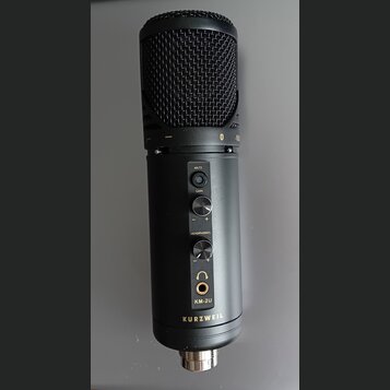 Černý kondenzátorový mikrofon s kovovou síťkou. Na těle jsou nápisy MUTE, GAIN a HEADPHONES u ovládacích prvků, dále označení modelu KM-2U a značka K…