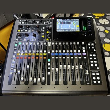 Digitální mixážní pult v černé barvě s řadou posuvníků, tlačítek a ovládacích knoflíků. V horní části je umístěn barevný displej a nápis X32 Compact.…
