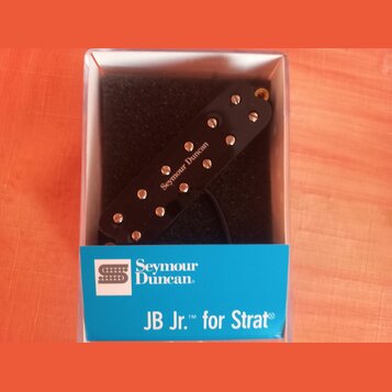 Černý humbucker snímač v plastovém průhledném boxu s modrou štítkem. Na krytce snímače je bílý nápis Seymour Duncan a na modrém štítku jsou loga a te…