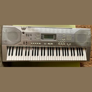 Stříbrný elektronický klavír značky CASIO, model CTK-800. Nástroj má plastové tělo s integrovanými reproduktory po stranách a digitálním displejem v…
