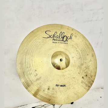 Zlatý mosazný činel typu ride s viditelným rýhováním povrchu. Na horní části je černý nápis „Schalloch Percussion Made in Germany“ a v dolní části ná…