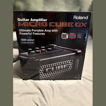 Kartonová krabice s kytarovým zesilovačem. Na povrchu je nápis Roland a model MICRO CUBE GX s textem Ultimate Portable Amp with Powerful Features. Js…