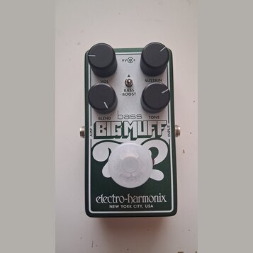Zelený efekt pedál s bílým nápisem bass BIG MUFF. Na horní části jsou čtyři černé ovládací knoflíky s popisky VOL, SUSTAIN, BLEND a TONE, dále nápis…