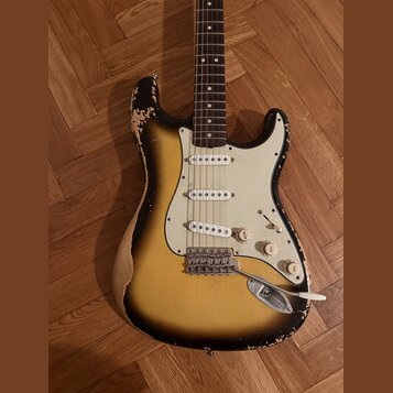 Elektrická kytara s tvarem Stratocaster, trojbarevným sunburst lakem a bílým pickguardem. Tělo vykazuje výrazné opotřebení v podobě rozestřeného laku…