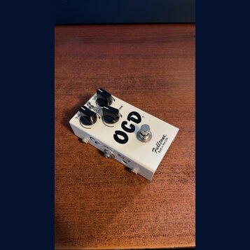 Bílý efekt pedál s nápisem OCD a značkou Fulltone Built in the USA. Na horní straně jsou tři černé ovládací knoflíky a jeden stomečový spínač. Na bok…