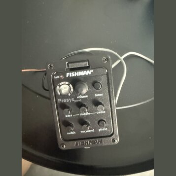 Černý plastový předzesilovač s integrovaným ladičkou a ovládacími prvky. Na zařízení jsou nápisy FISHMAN®, batt, volume, tuner, Presys blend, bass, m…