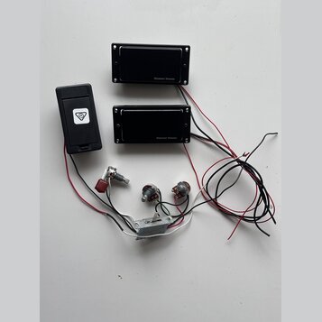 Dva černé humbuckery s nápisem Seymour Duncan, jeden černý plastový box s bílým logem v trojúhelníku a sada elektroniky. Soubor obsahuje dva potencio…