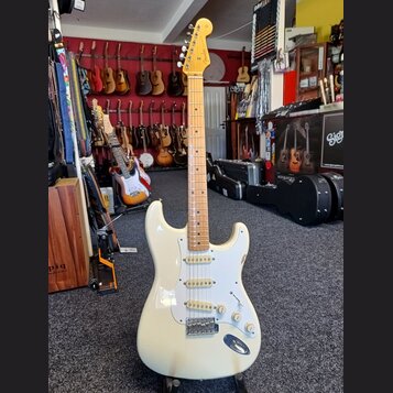 Elektrická kytara typu Stratocaster v krémové barvě s bílým pickguardem a hnedým javorovým hmatníkem. Na hlavě je vidět nápis Fender. Kytara má tři s…