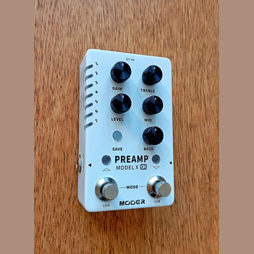 Bílý efekt pedál s nápisy PREAMP, MODEL X (X2) a značkou MOOER. Zařízení má pět černých otočných potenciometrů s popisky GAIN, TREBLE, LEVEL, MID a B…