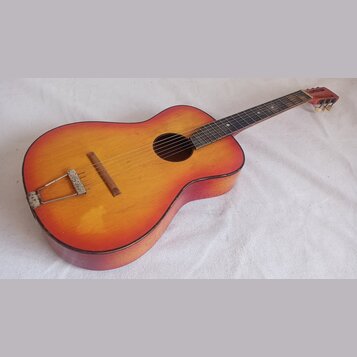 Akustická kytara s žlutě-oranžovým přechodem barvy (sunburst) na deskách a tmavě hnědými boky. Nástroj vykazuje známky opotřebení v podobě škrábanců…
