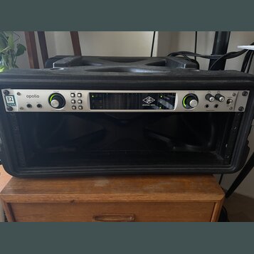 Černý rackový kufřík, v němž je osazen stříbrný zvukový interface. Na zařízení jsou nápisy apollo, UA UNIVERSAL AUDIO a logo 32 QUAD. Přední panel ob…