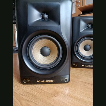Dva černé studiové monitory s Kevlarovými membránami v béžové barvě. Na spodní hraně je uveden nápis M-AUDIO a vlevo označení SPEAKER MODES s možnost…