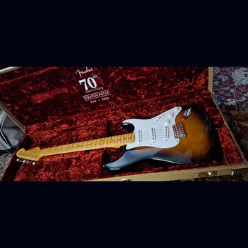 Elektrická kytara typu Stratocaster v barvě sunburst s bílým pickguardem a javorovým hmatníkem leží v otevřeném tvrdém kufru s červeným plyšovým vnit…