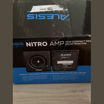 Fotografie zachycuje kartonovou krabici s produktem Alesis Nitro Amp. Na přední straně je nápis NITRO AMP 70W COMPACT PER DRUM MONITOR a obrázky dvou…