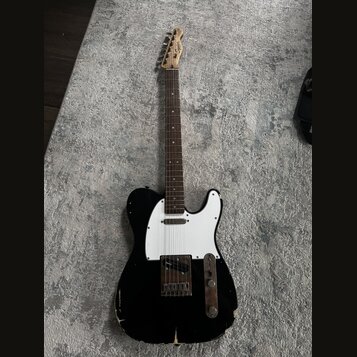 Černá elektrická kytara typu Telecaster s bílým pickguardem a hnědým hmatníkem. Na hlavě je viditelné logo Squier. Instrument vykazuje výrazné opotře…