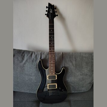 Černá elektrická kytara s bílým lemováním korpusu a hmatníku stehového dřeva. Na hlavě je bílý nápis Cort. Nástroj má konfiguraci dvou humbuckerů a j…