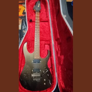Elektrická kytara s tmavým, kovovým povrchem v červeně vystlaném tvrdém kufru. Na hlavě hmatníku je vidět nápis "ESP". Kytara má dva humbuckery, trem…