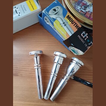 Tři stříbrné trubkové munzpísty položené na dřevěném povrchu. Na levém je nápis "JET-TONE", uprostřed nápisy "LBR" a "GLN" a vpravo nápis "VINCENT BA…