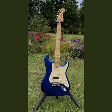 Modrá elektrická kytara typu Stratocaster s krčkem a hmatníkem ze světlého dřeva. Na hlavě je viditelné logo Fender. Kytara má krémový pickguard, tři…