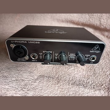 Černý audio rozhraní s kovovým předním panelem. Na horní hraně a vpravo je logo a nápis behringer, vlevo nápis U-PHORIA UMC22. Na předním panelu jsou…