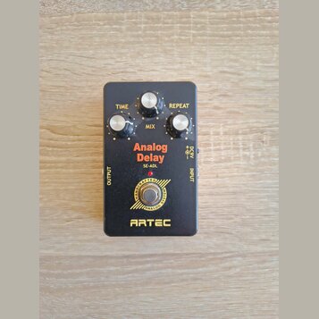 Černý efekt pedál s nápisy Analog Delay, SE-ADL a ARTEC. Obsahuje tři bílé ovládací knoflíky s popisky TIME, MIX a REPEAT. V dolní části je kruhové l…