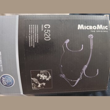 Fotografie znázorňuje krabici od mikrofonu. Na černé části obalu je bílý nápis MicroMic THE ORIGINAL, model C 520 VOCAL a texty v několika jazycích z…