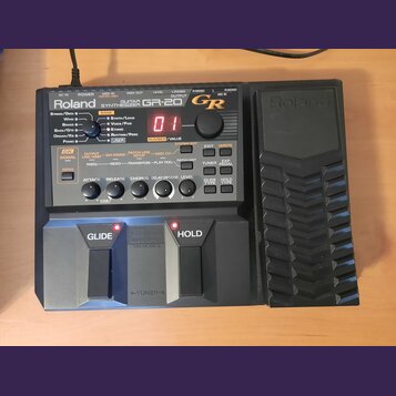 Černý kytarový syntetizátor Roland GR-20. Na předním panelu jsou vidět nápisy Roland, GUITAR SYNTHESIZER a GR-20 s červeným digitálním displejem zobr…