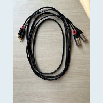 Dva černé audio kabely s konektory typu XLR na jedné straně a RCA na druhé. Na kabelích je vidět bílý nápis AUDIO CABLE a MODEL. Konektory RCA jsou v…